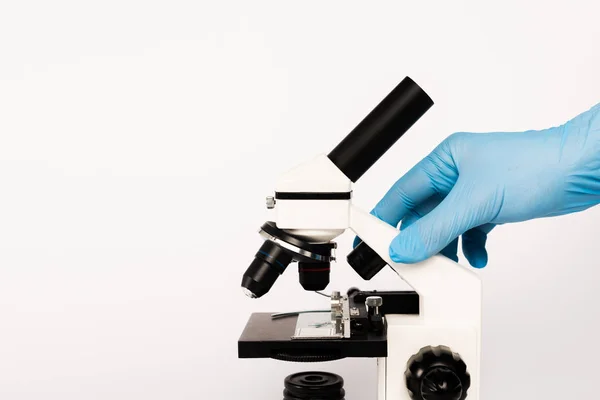 Visão recortada do cientista em luva de látex tocando microscópio isolado em branco — Fotografia de Stock