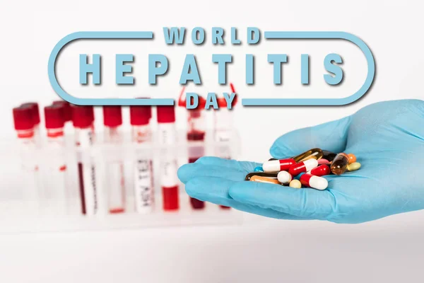 Обрізаний вид вченого в латексній рукавичці, що тримає таблетки біля пробірки і Всесвітній день гепатиту на білому — стокове фото