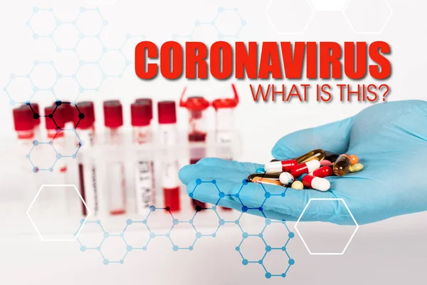 Cropped view of scientist in latex glove holding pills near test tubes and coronavirus what is this lettering on white — Stock Photo