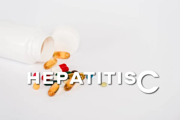 Пляшка поблизу барвистих таблеток і гепатиту С на білому — стокове фото