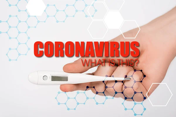 Vista recortada de la mujer sosteniendo termómetro digital cerca de coronavirus lo que es esta inscripción en blanco - foto de stock