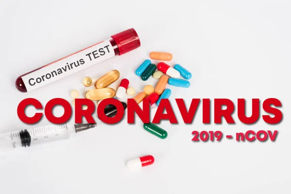 Bunte Pillen in der Nähe der Probe mit Coronavirus-Test, Spritze und Coronavirus 2019-ncov Schriftzug auf weiß — Stockfoto