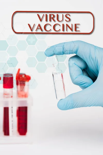 Vista recortada de un científico sosteniendo un frasco de vidrio con líquido cerca de los tubos de ensayo y letras de vacunas contra el virus en blanco - foto de stock