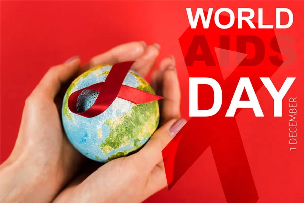 Cropped view of woman holding globe with red ribbon near world aids day lettering on red — Stock Photo