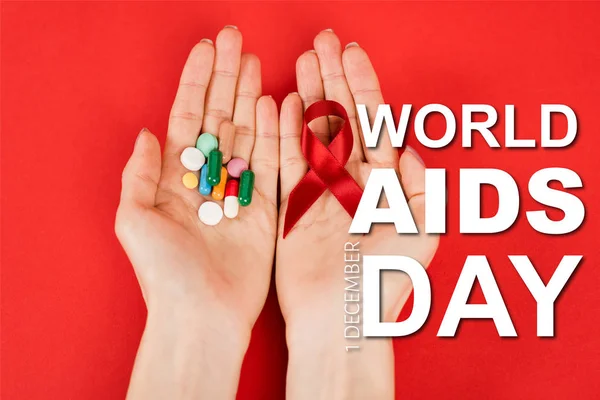 Top view of woman holding red ribbon and pills near world aids day lettering on red — Stock Photo