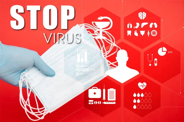 Vista ritagliata di scienziato in possesso di maschere mediche vicino fermata lettering virus sul rosso — Stock Photo