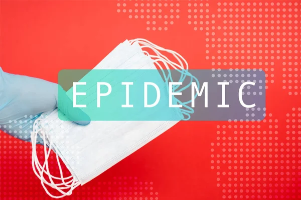 Cropped view of scientist holding medical masks near epidemic lettering on red — Stock Photo