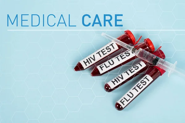 Вид сверху шприца на образцах с тестом на ВИЧ и грипп рядом с надписью медицинской помощи на синем — стоковое фото
