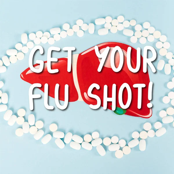Vue du dessus des pilules près du foie dessiné et obtenez votre lettrage de vaccin contre la grippe sur bleu — Photo de stock