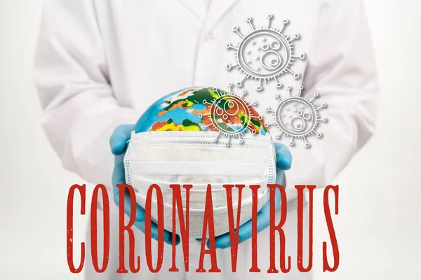 Vista ritagliata dello scienziato che tiene globo in maschera protettiva vicino coronavirus lettering su bianco — Foto stock