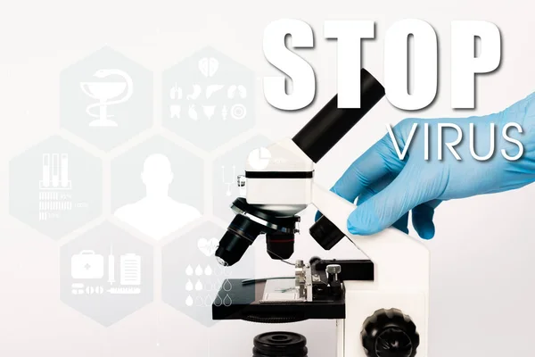 Vista cortada do cientista em luva de látex tocando microscópio perto de parar de lettering vírus no branco — Fotografia de Stock