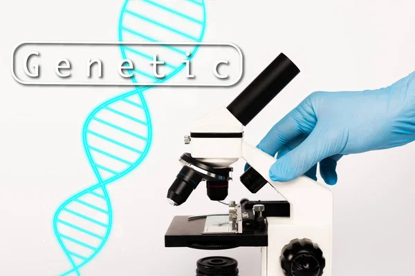 Vista cortada do cientista em luva de látex tocando microscópio perto de letras genéticas em branco — Fotografia de Stock
