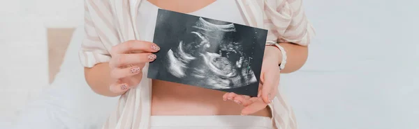 Cropped view of pregnant woman holding ultrasound scan of baby on bed, panoramic shot — Stock Photo