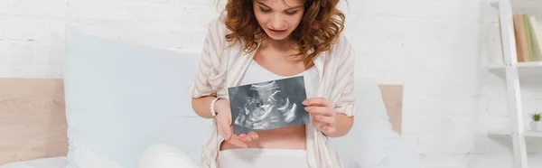 Panoramic shot of pregnant woman holding ultrasound scan of baby on bed — Stock Photo