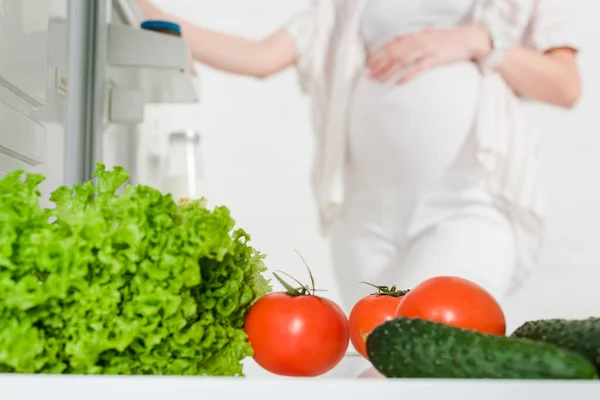 Selektiver Fokus der schwangeren Frau beim Öffnen des Kühlschranks mit frischem Gemüse isoliert auf Weiß — Stockfoto