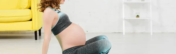 Vista cortada da mulher grávida em sportswear sentado no chão na sala de estar, tiro panorâmico — Fotografia de Stock