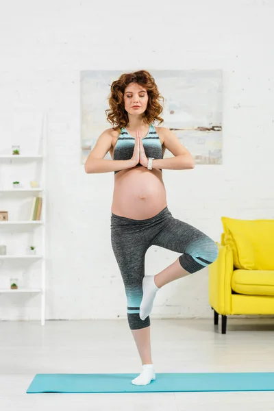 Красива вагітна жінка в йозі позує на фітнес килимок у вітальні — стокове фото