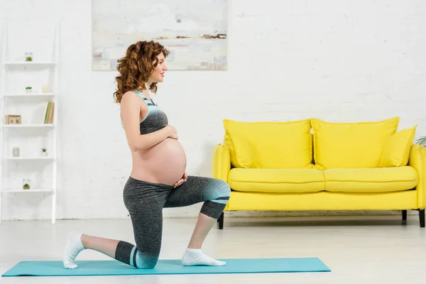 Side view of smiling pregnant woman exercising on fitness mat in living room — Stock Photo