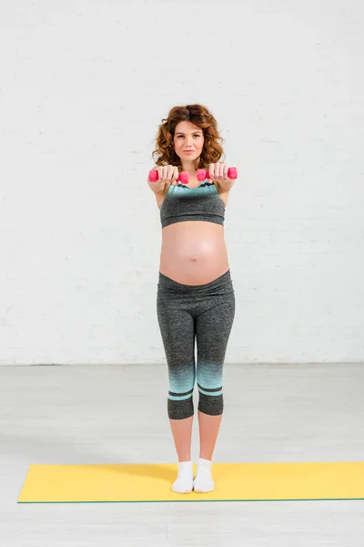 Beautiful pregnant woman training with dumbbells on fitness mat at home — Stock Photo