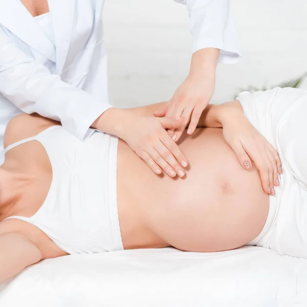 Vista cortada do massagista fazendo massagem na barriga para a mulher grávida na mesa de massagem — Fotografia de Stock