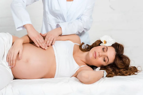 Masseur macht Bauchmassage für schwangere Frau mit Orchidee im Haar im Wellnesszentrum — Stockfoto