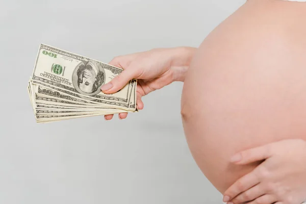 Vista cortada da mulher grávida segurando notas de dólar em fundo cinza, conceito de maternidade de substituição — Fotografia de Stock