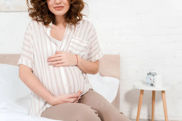 Ausgeschnittene Ansicht einer schwangeren Frau, die ihren Bauch auf dem Bett berührt — Stockfoto