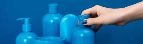 Plan panoramique de femme tenant bouteille avec shampooing sur fond bleu — Photo de stock