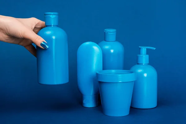 Vue recadrée de la femme tenant bouteille avec shampooing sur fond bleu — Photo de stock