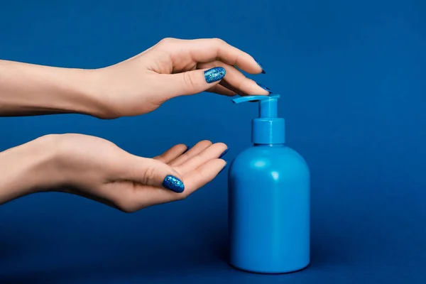 Cropped view of woman pumping out liquid soap on blue background — Stock Photo