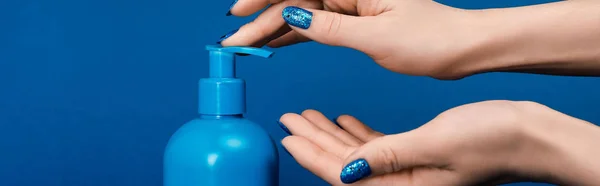 Tiro panorámico de la mujer bombeo de jabón líquido aislado en azul - foto de stock