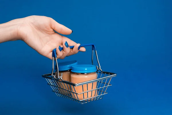 Vue recadrée de la femme tenant panier avec de la nourriture pour bébé dans des pots sur fond bleu — Photo de stock