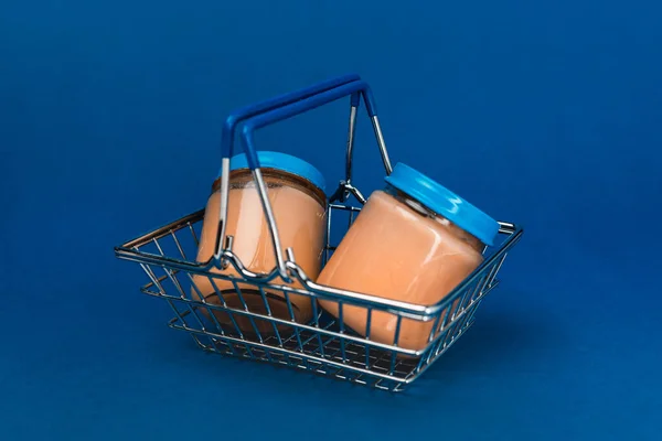 Банки с детским питанием в корзине для покупок на голубом фоне — стоковое фото
