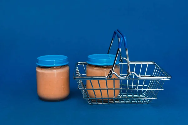 Gläser mit Babynahrung und Einkaufskorb auf blauem Hintergrund — Stockfoto
