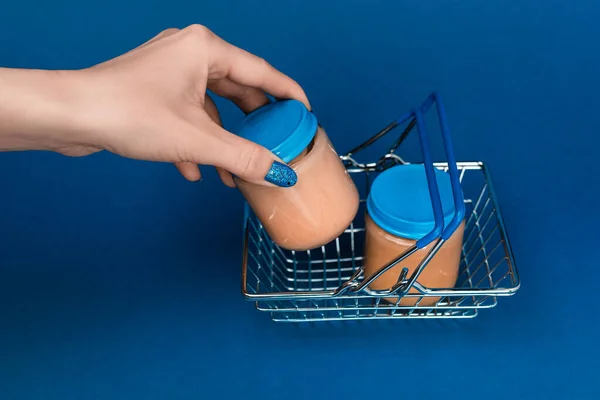 Vista cortada da mulher colocando no frasco cesta de compras com comida de bebê no fundo azul — Fotografia de Stock