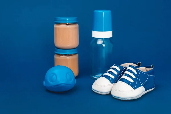 Baby bottle, toy, baby shoes, jar with baby food ob blue background — Stock Photo