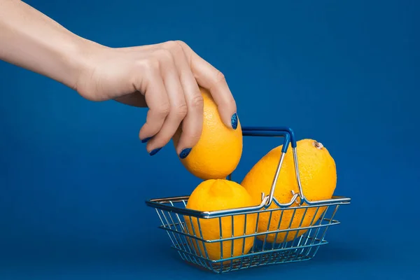 Vue recadrée de femme mettant citron dans le panier sur fond bleu — Photo de stock