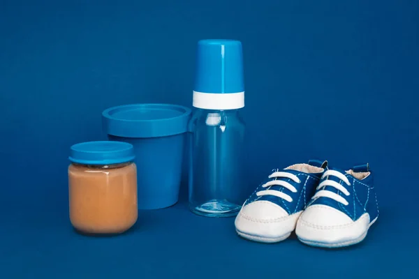 Eimer, Babyflasche, Babyschuhe, Glas mit Babynahrung auf blauem Hintergrund — Stockfoto