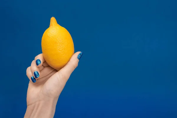Vista recortada de la mujer sosteniendo limón entero aislado en azul - foto de stock