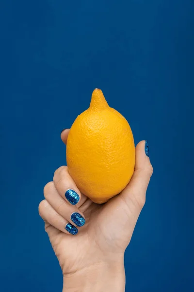 Vista cortada de mulher segurando limão inteiro isolado em azul — Fotografia de Stock
