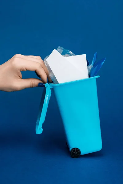 Cropped view of woman holding toy trash can on blue background — Stock Photo