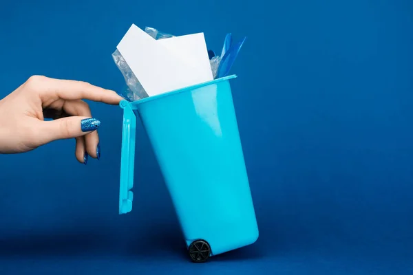 Vista recortada de la mujer tocando bote de basura de juguete sobre fondo azul - foto de stock