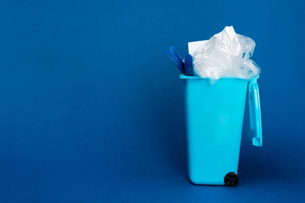 Toy trash can with rubbish on blue background with copy space — Stock Photo