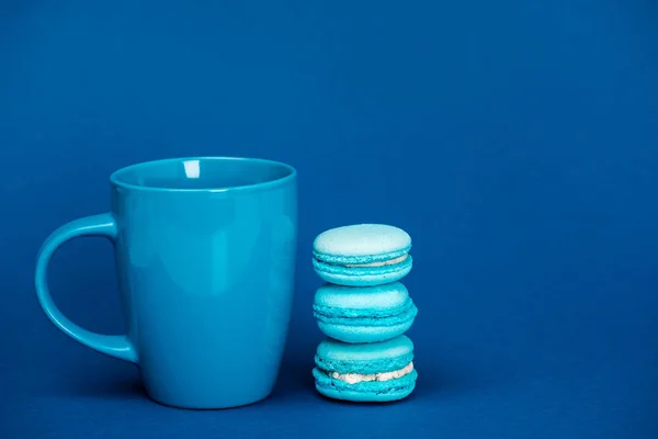 Saborosos macaroons franceses e xícara no fundo azul com espaço de cópia — Fotografia de Stock