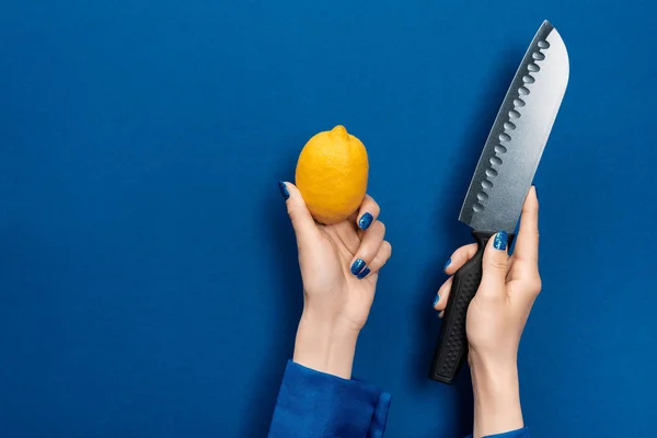 Vista recortada de la mujer sosteniendo limón y cuchillo sobre fondo azul - foto de stock