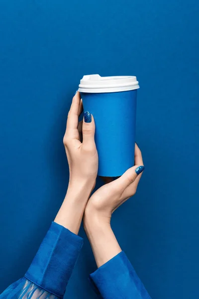 Vista recortada de la mujer sosteniendo taza de papel sobre fondo azul — Stock Photo