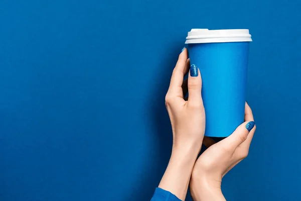 Vista ritagliata della donna che tiene tazza di carta su sfondo blu — Foto stock