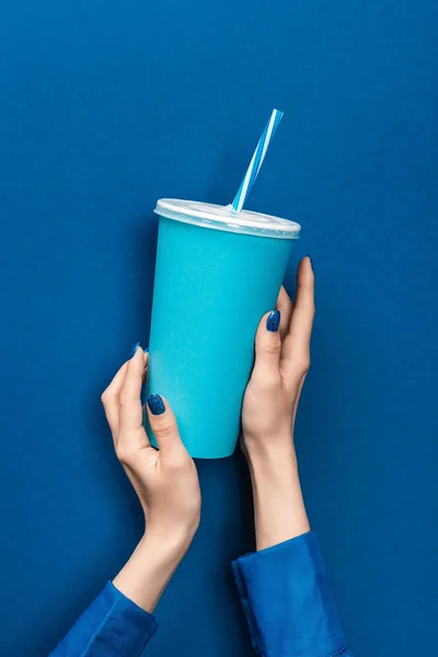 Vista recortada de la mujer sosteniendo taza de papel sobre fondo azul - foto de stock