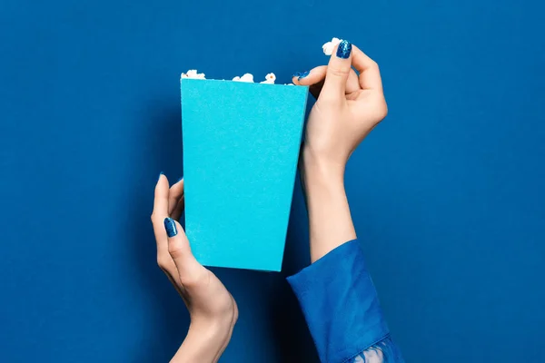 Corte vista de mulher segurando caixa com pipoca no fundo azul — Fotografia de Stock