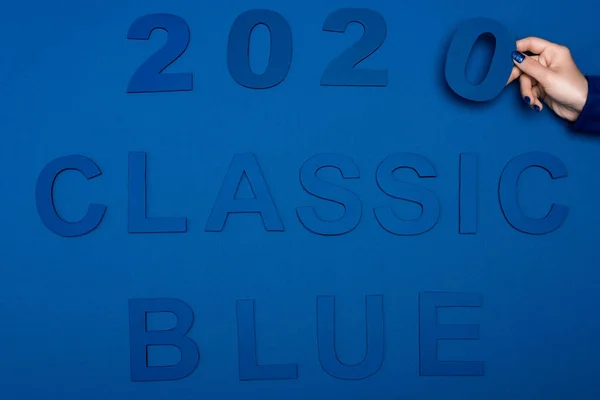 Cropped view of woman holding number near classic blue lettering on blue background — Stock Photo